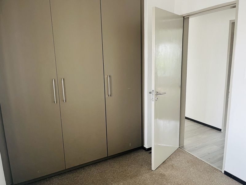 A bedroom featuring built-in cupboards and a doorway leading to an adjacent room with laminate flooring.