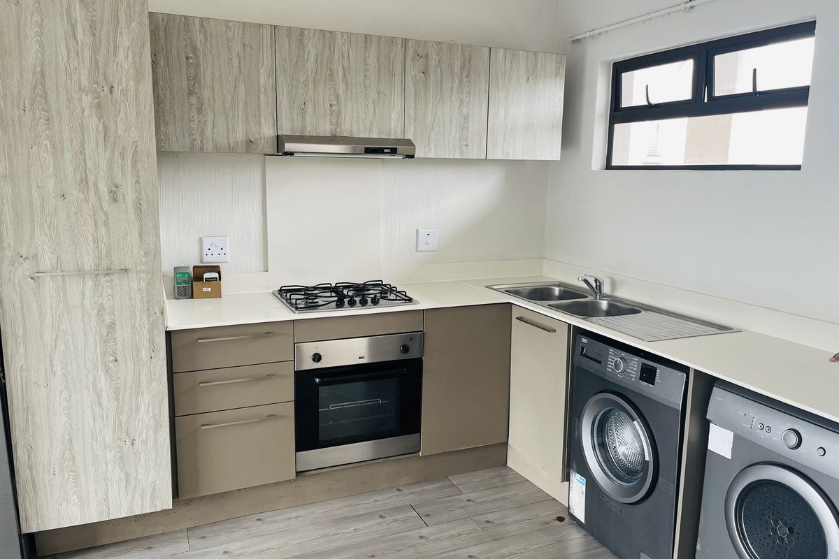Modern kitchen featuring light wood-grain cabinetry, stone countertops, a gas hob, built-in oven, extractor fan, and integrated laundry appliance connections.