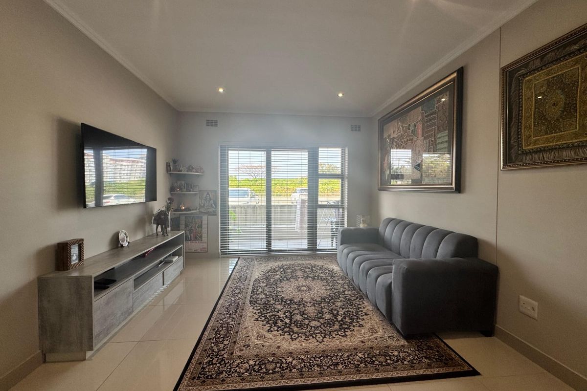 A well-maintained living room featuring neutral tiled flooring, recessed downlighting, and a large sliding glass door with venetian blinds providing natural light.