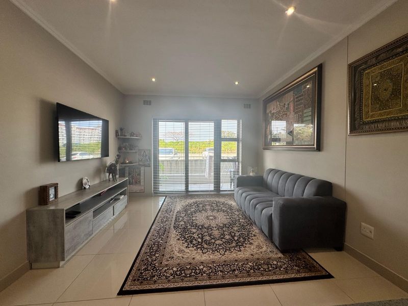 A well-maintained living room featuring neutral tiled flooring, recessed downlighting, and a large sliding glass door with venetian blinds providing natural light.