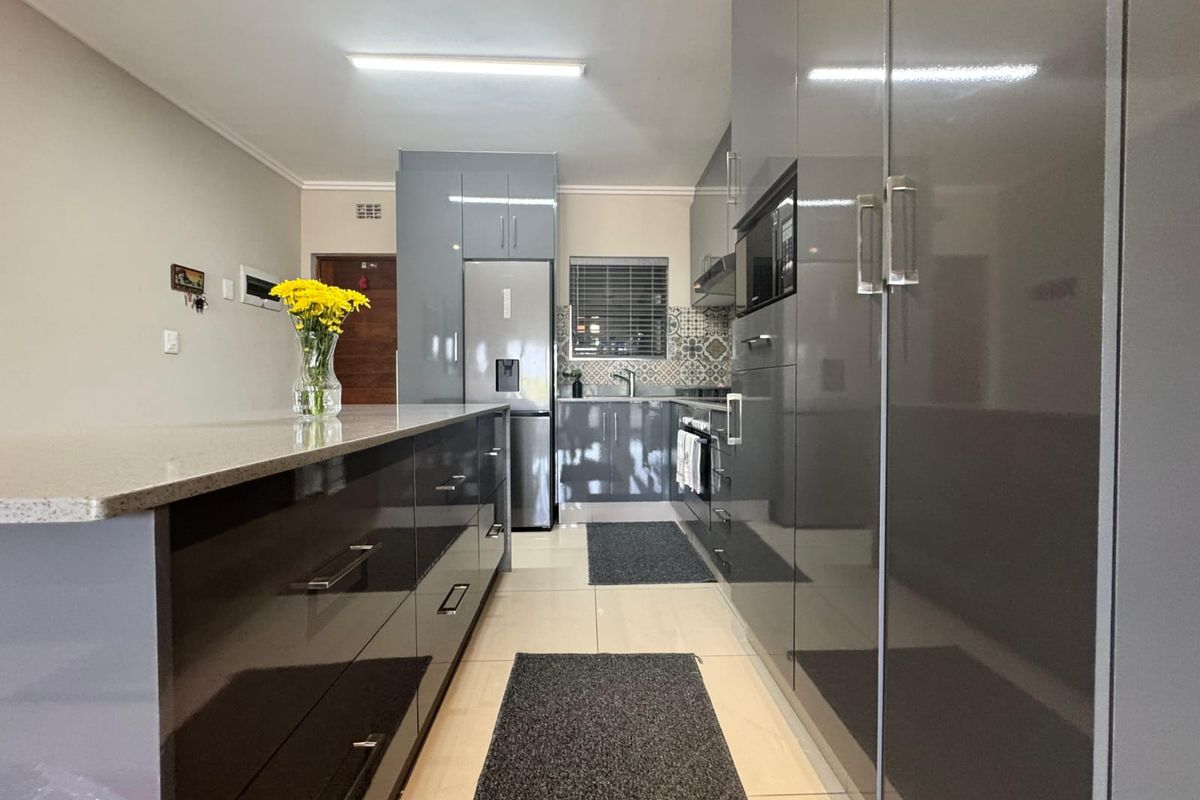 Modern kitchen featuring high-gloss grey cabinetry, stone countertops, integrated appliances, and a stylish tiled backsplash with neutral floor tiles.
