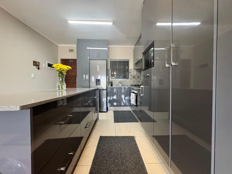 Modern kitchen featuring high-gloss grey cabinetry, stone countertops, integrated appliances, and a stylish tiled backsplash with neutral floor tiles.