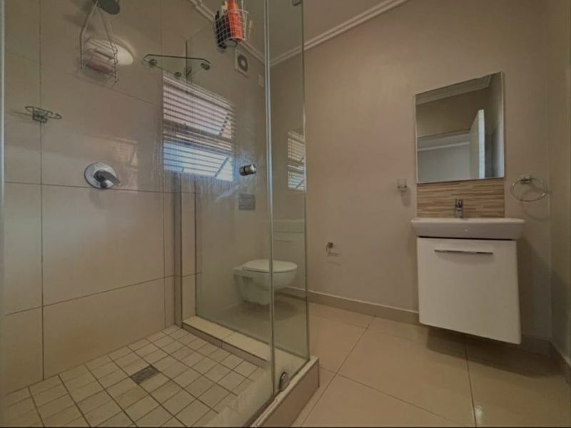 A clean, modern bathroom featuring a glass-enclosed shower, wall-mounted vanity with basin, and a wall-mounted toilet with neutral tiled finishes.