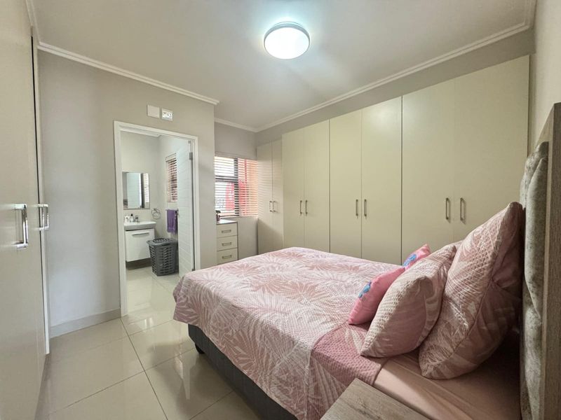 A well-maintained bedroom featuring extensive built-in cupboards, tiled flooring, and an adjoining en-suite bathroom with modern fixtures.