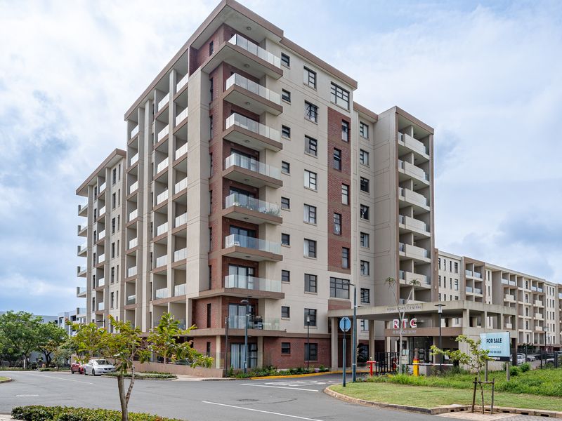 A modern multi-story apartment complex featuring a brick and concrete facade, glass-fronted balconies, and a covered entrance area with signage.