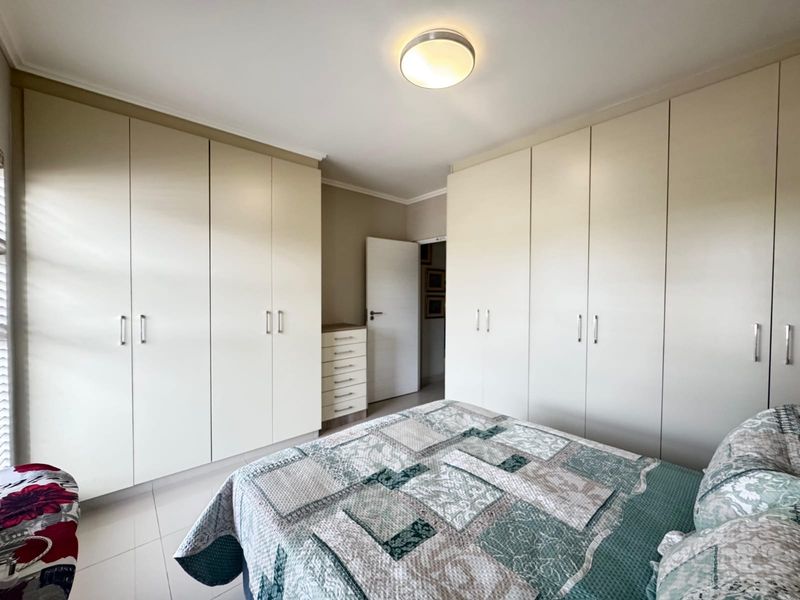 A well-maintained bedroom featuring extensive built-in cupboards providing ample storage space and neutral tiled flooring.
