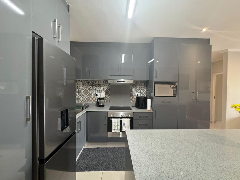 Modern kitchen featuring high-gloss grey cabinetry, stone countertops, a patterned tile backsplash, and integrated appliances including an oven, hob, and microwave.