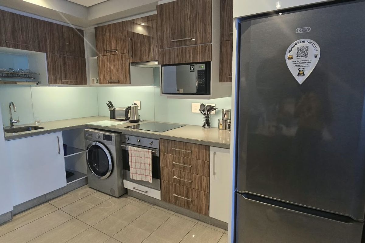 Modern kitchen featuring wood-grain and white cabinetry, stone countertops, glass splashback, and integrated appliances including an oven, hob, and microwave.
