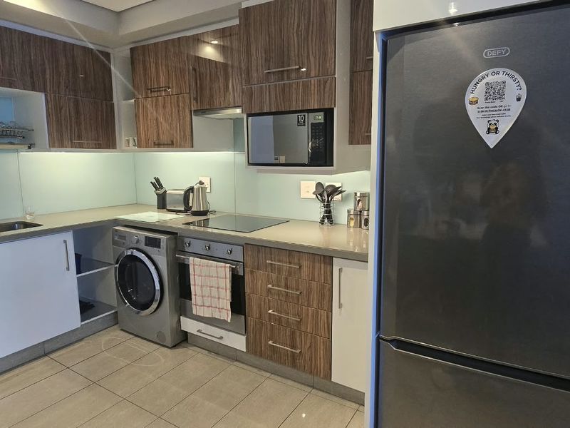 Modern kitchen featuring wood-grain and white cabinetry, stone countertops, glass splashback, and integrated appliances including an oven, hob, and microwave.