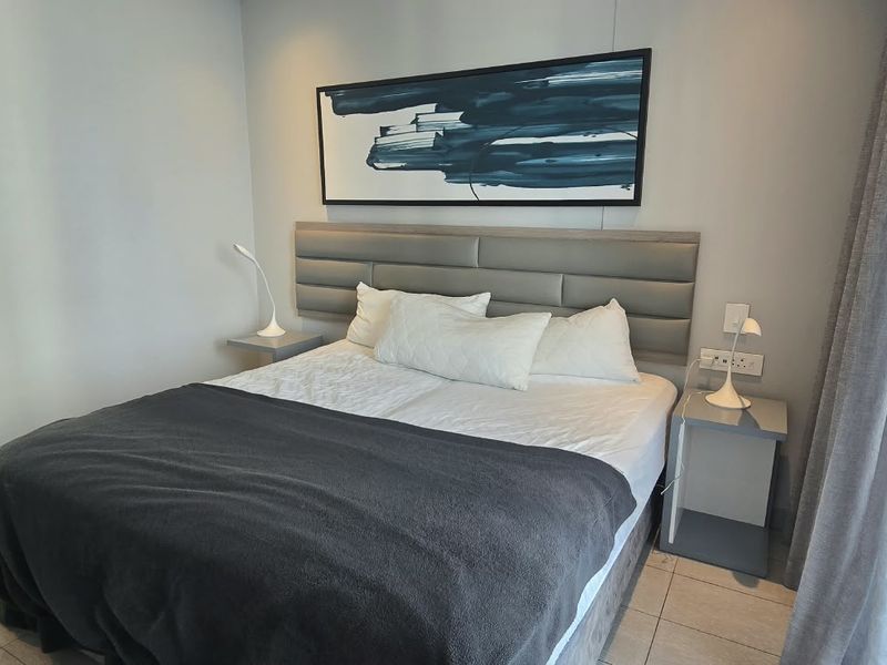 A modern, well-maintained bedroom featuring tiled flooring, a built-in headboard, and direct access to a balcony through a sliding glass door.