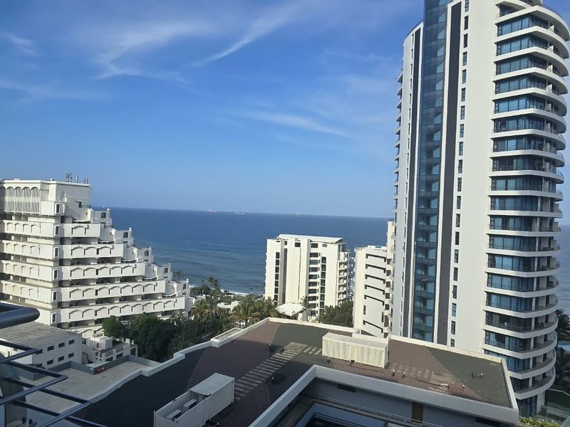 A high-level coastal view overlooking surrounding apartment buildings and the ocean, captured from a balcony.