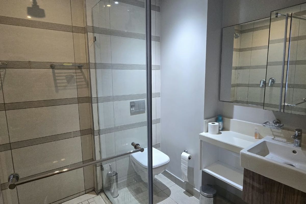 Modern bathroom featuring a glass-enclosed shower, wall-mounted toilet, vanity basin with storage, and a mirrored medicine cabinet.