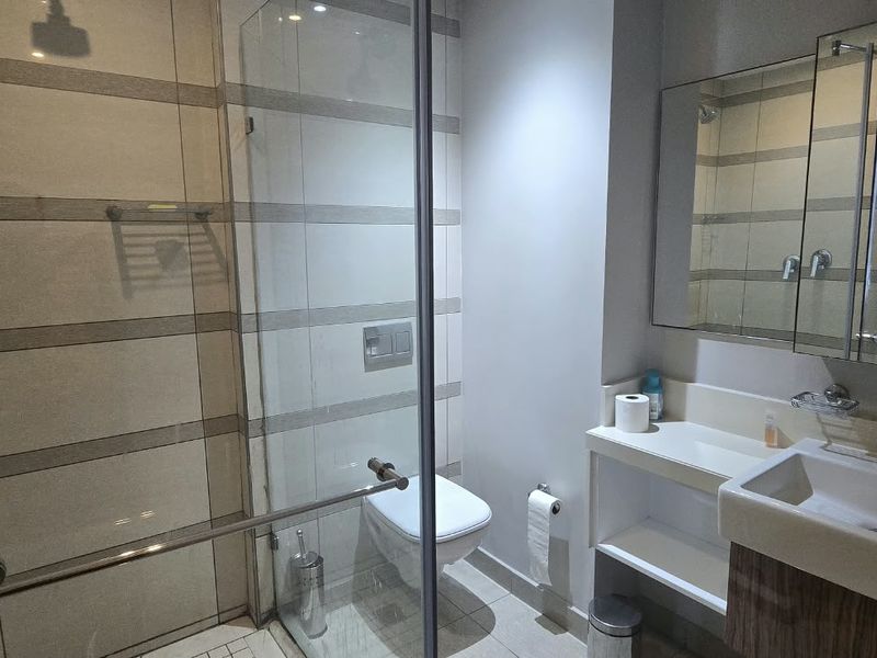 Modern bathroom featuring a glass-enclosed shower, wall-mounted toilet, vanity basin with storage, and a mirrored medicine cabinet.