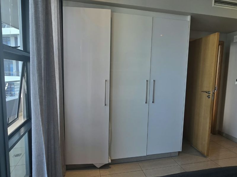 A modern bedroom featuring built-in white cupboards, tiled flooring, and direct access to a balcony with ocean views and an en-suite bathroom.