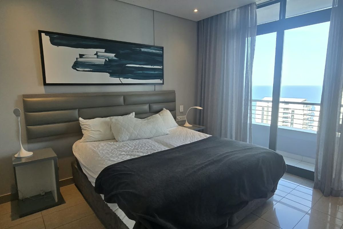A modern bedroom featuring tiled flooring, a built-in headboard, and large sliding glass doors that open to a balcony with ocean views.