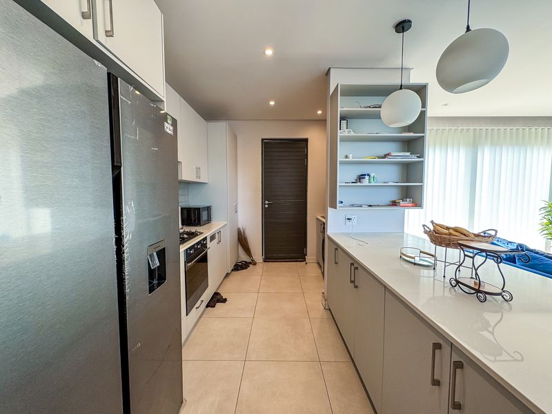 Modern kitchen featuring sleek cabinetry, stone countertops, integrated appliances, and a functional layout with a breakfast bar and contemporary lighting.