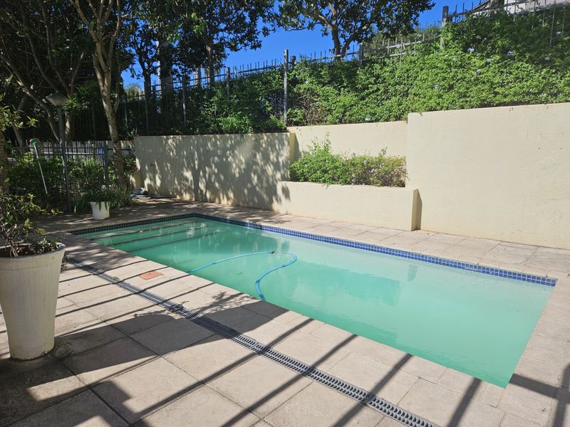 A private outdoor swimming pool area featuring a tiled surround, retaining wall, and perimeter fencing, offering a functional space for outdoor recreation.