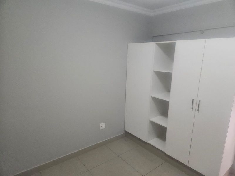 A clean, neutral bedroom featuring tiled flooring and a modern white built-in wardrobe with open shelving.