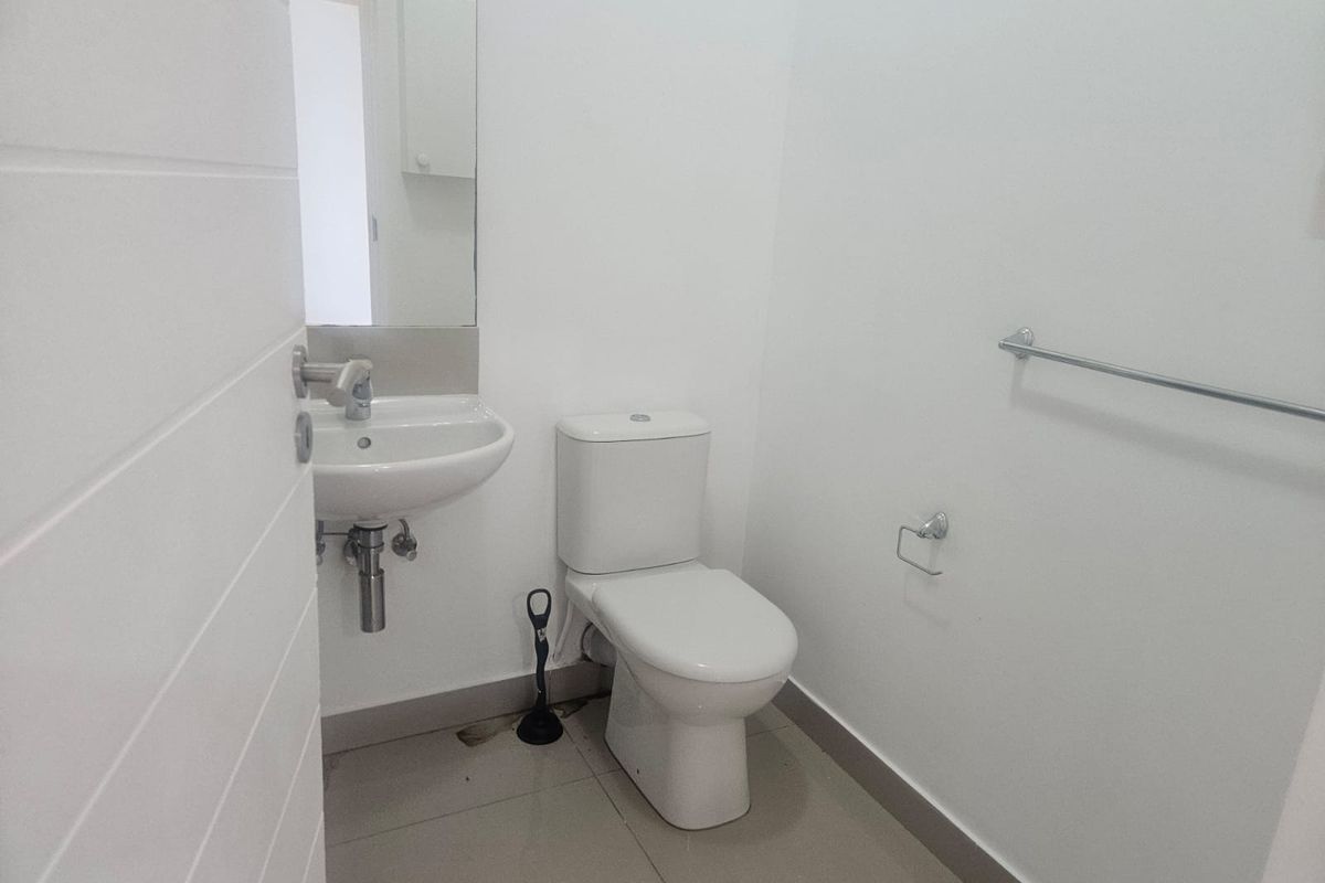 A compact, minimalist bathroom featuring a wall-mounted basin, a standard toilet, and neutral floor tiling.