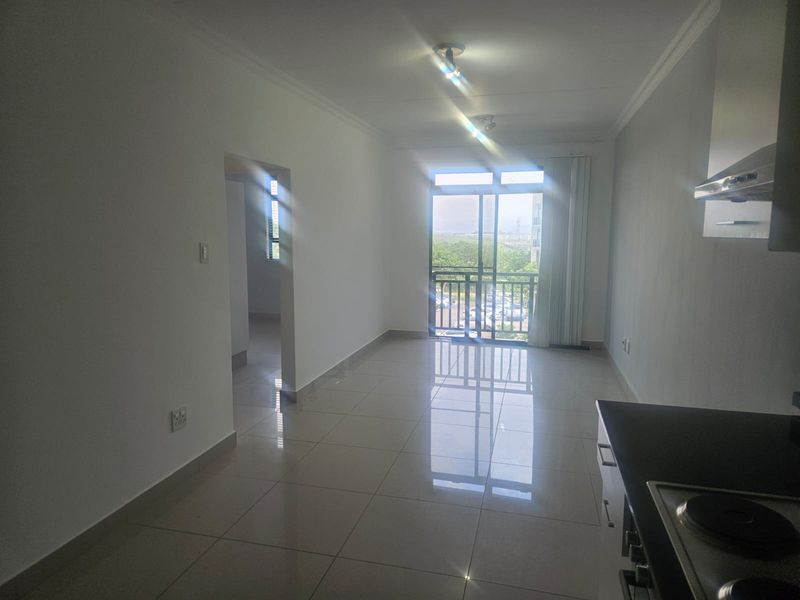 Bright open-plan living area featuring tiled floors, a modern kitchen with built-in appliances, and a sliding door leading to a balcony.