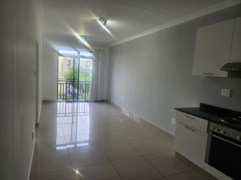 An open-plan living and kitchen area featuring tiled floors, modern white cabinetry with granite countertops, and a sliding door leading to a balcony.