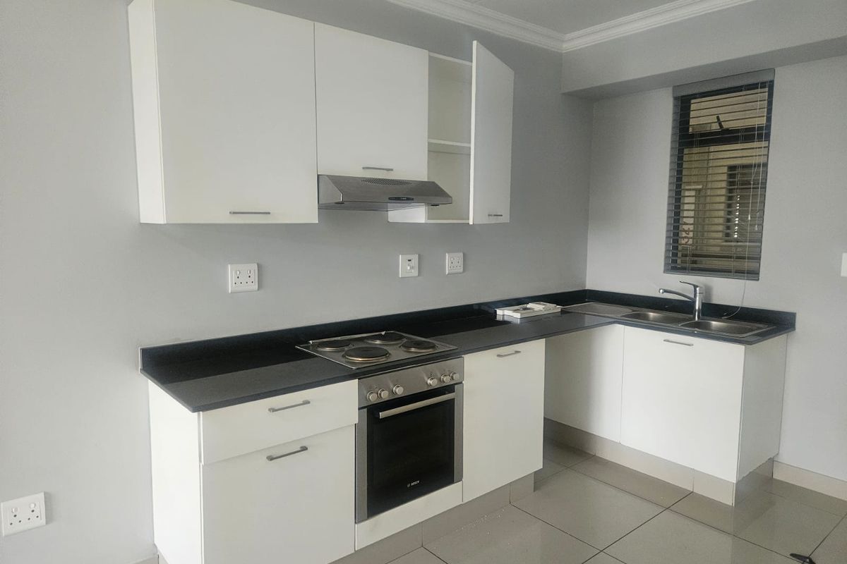 A clean, modern kitchen featuring white cabinetry, dark stone countertops, built-in oven, electric hob, and a double sink with a mixer tap.