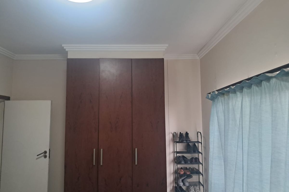 A bedroom featuring dark wood built-in cupboards and decorative ceiling cornicing.