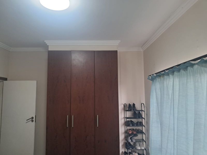 A bedroom featuring dark wood built-in cupboards and decorative ceiling cornicing.