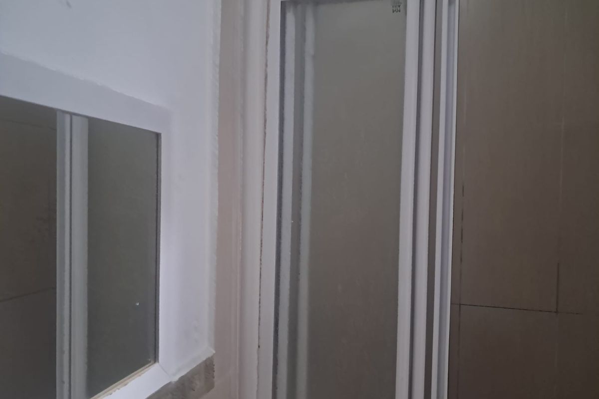 A bathroom interior featuring a shower enclosure, wall mirror, and tiled wall finishes, currently in need of maintenance and cosmetic updates.
