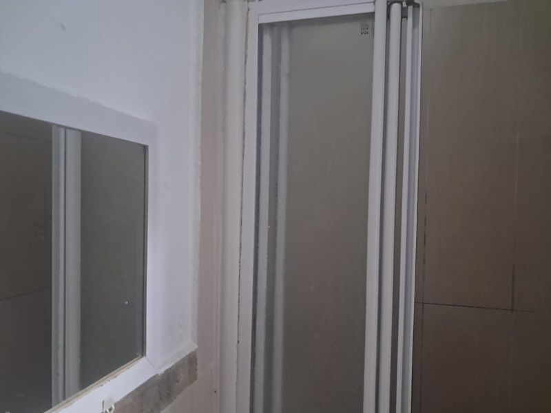 A bathroom interior featuring a shower enclosure, wall mirror, and tiled wall finishes, currently in need of maintenance and cosmetic updates.