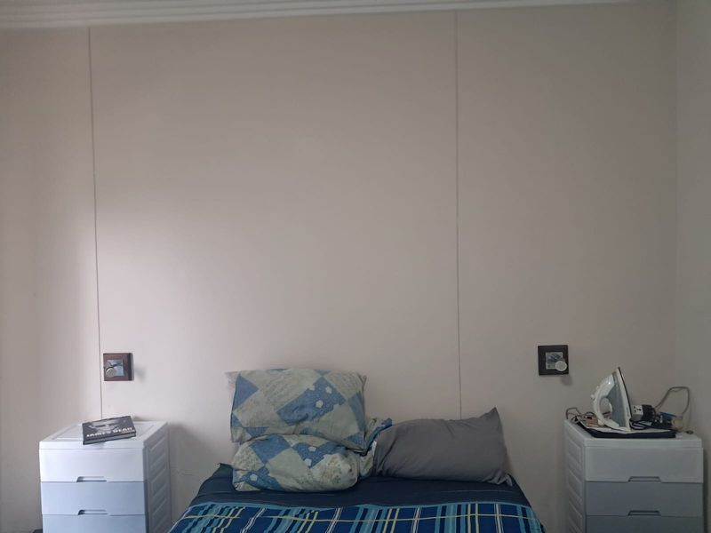 A simple bedroom featuring neutral walls, coving, and integrated wall-mounted light switches on either side of the bed area.