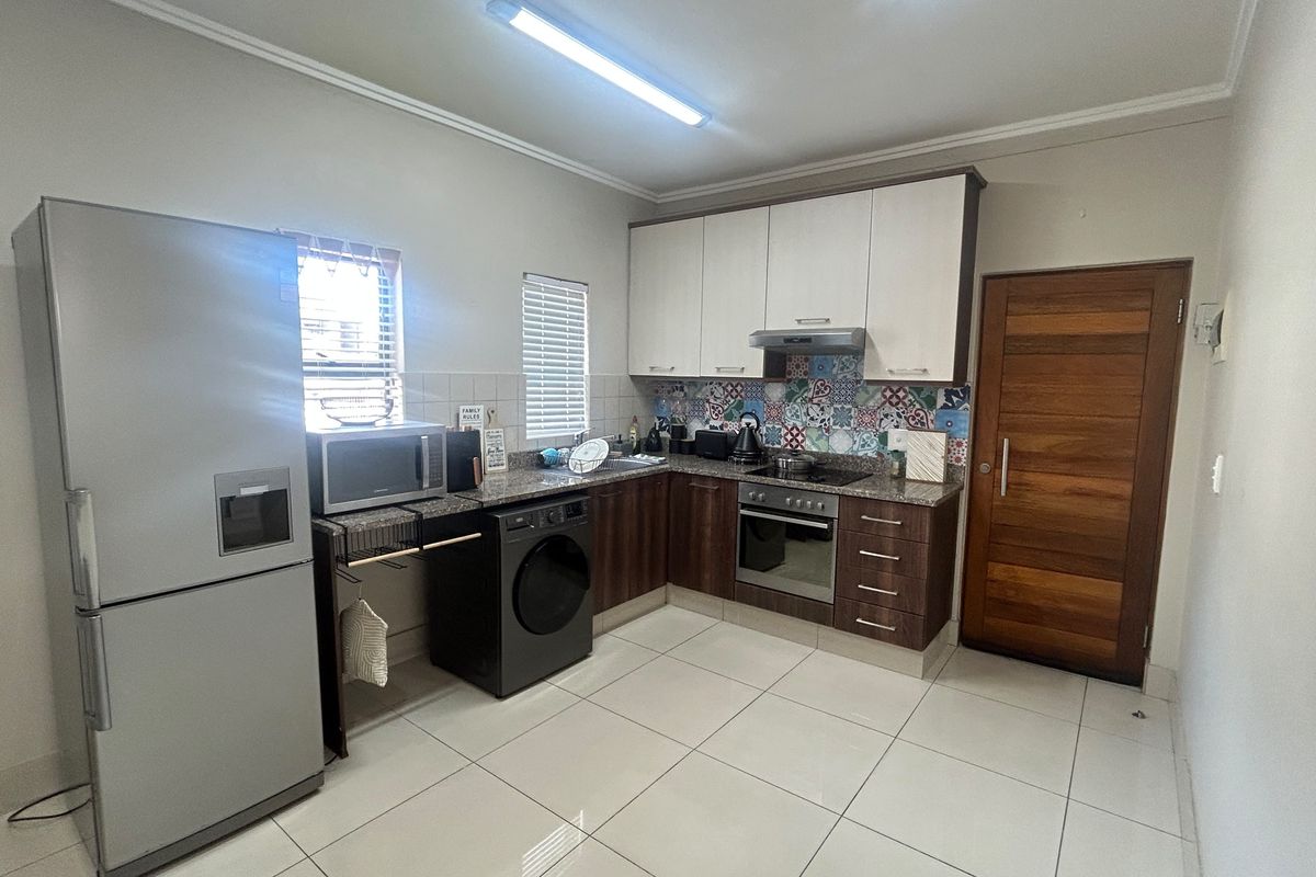 A functional kitchen featuring modern two-tone cabinetry, granite countertops, a tiled backsplash, and integrated appliances including an oven and hob.