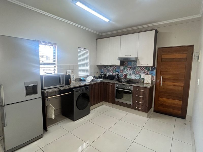 A functional kitchen featuring modern two-tone cabinetry, granite countertops, a tiled backsplash, and integrated appliances including an oven and hob.