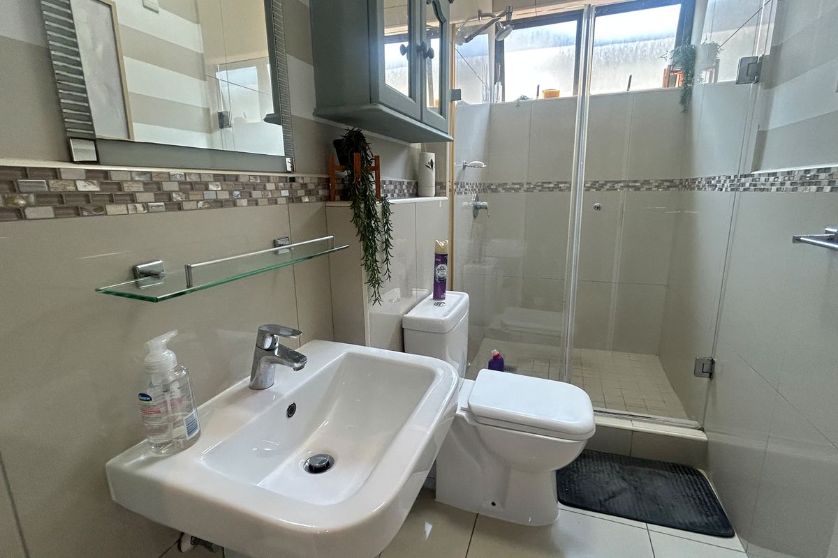 A functional bathroom featuring a wall-mounted basin, glass-enclosed shower, and neutral tiled finishes with a decorative mosaic border.