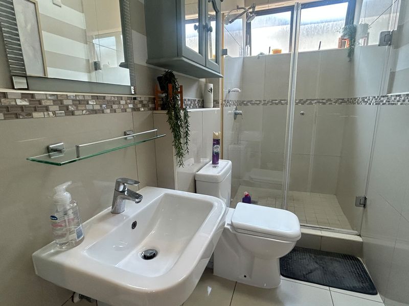 A functional bathroom featuring a wall-mounted basin, glass-enclosed shower, and neutral tiled finishes with a decorative mosaic border.