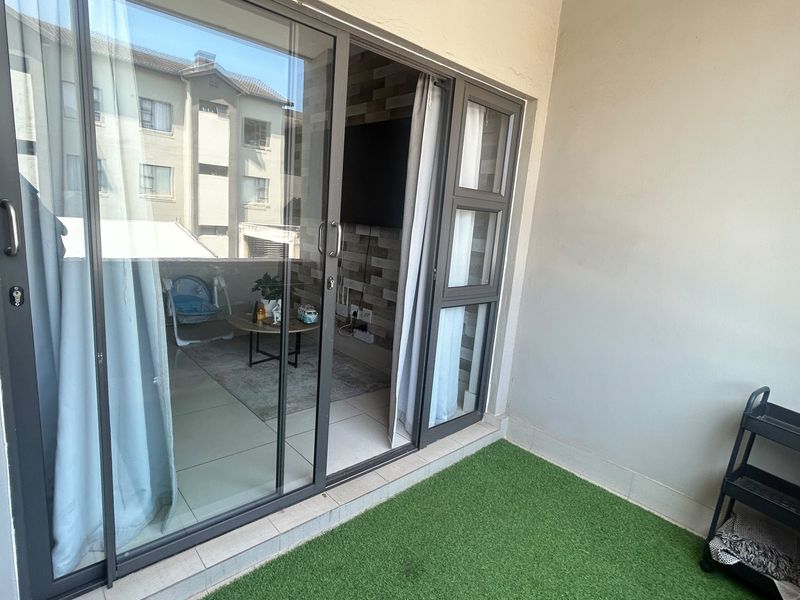 A compact balcony featuring artificial grass flooring and modern aluminium sliding doors providing access to the interior living space.