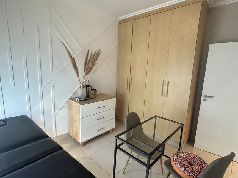 A well-maintained bedroom featuring light wood built-in wardrobes, modern tiled flooring, and a stylish geometric feature wall.