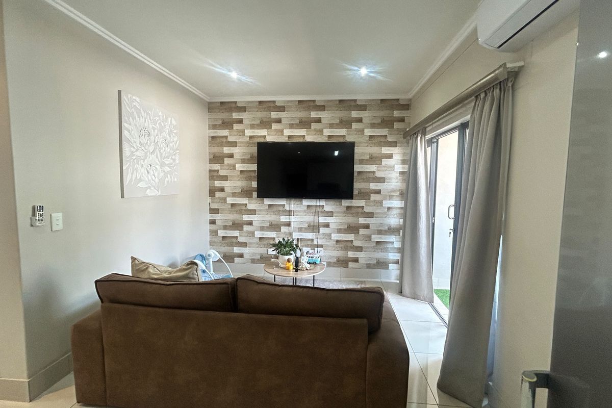 A well-maintained living room featuring a textured feature wall, tiled flooring, recessed lighting, and a sliding glass door providing access to the outdoor area.