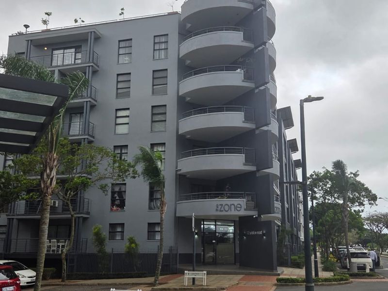 A modern multi-story apartment building featuring a grey facade, distinctive curved balconies, and a prominent glass entrance area.