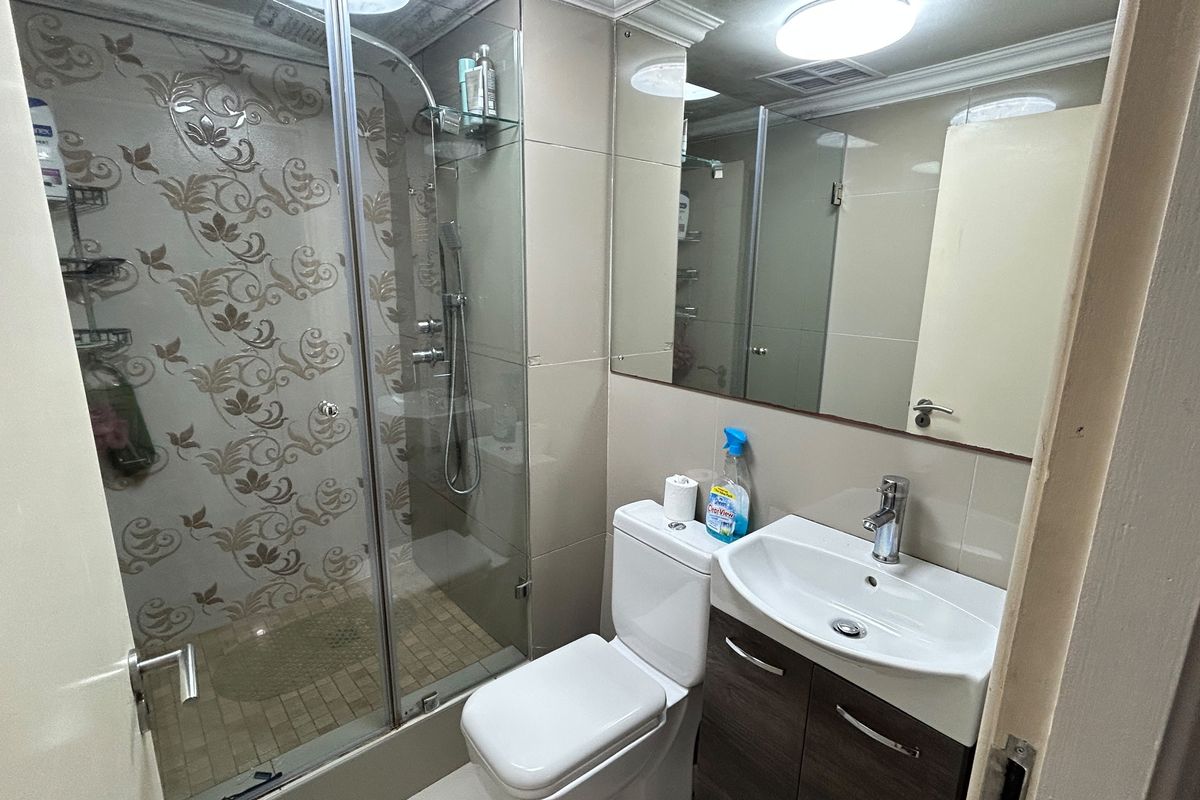 A functional bathroom featuring a glass-enclosed shower, vanity cabinet with basin, and wall-mounted mirror with neutral tiled finishes.