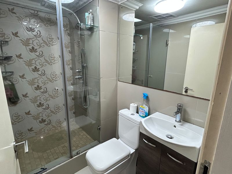 A functional bathroom featuring a glass-enclosed shower, vanity cabinet with basin, and wall-mounted mirror with neutral tiled finishes.