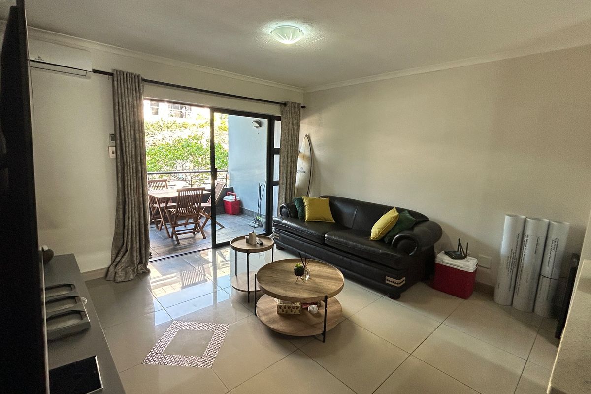 A bright living room featuring large sliding glass doors that open onto a private balcony, complemented by neutral tiled flooring and air conditioning.