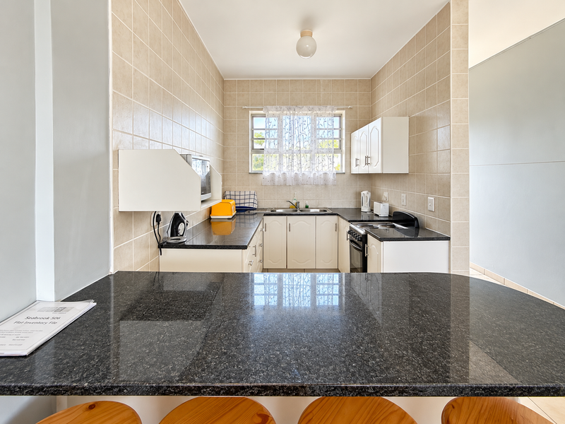 A functional kitchen featuring granite countertops, a breakfast bar, tiled walls, and built-in cabinetry with a freestanding stove.