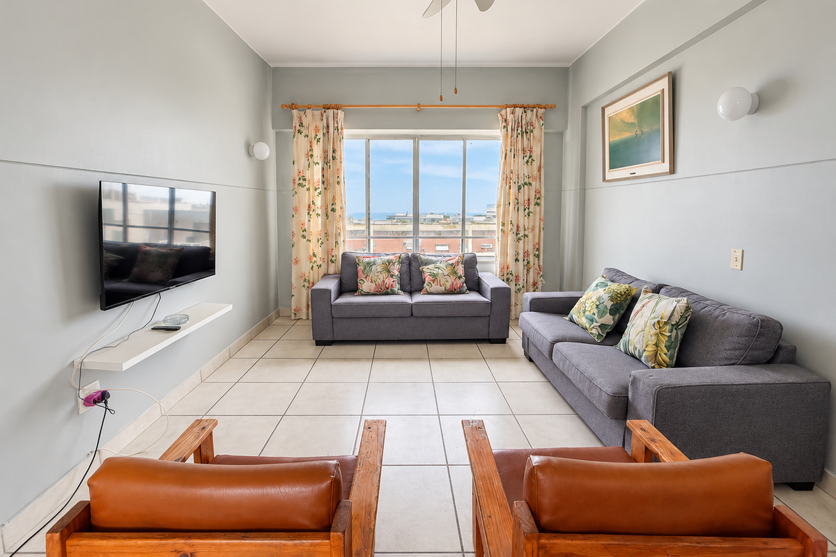 A bright living room featuring tiled flooring, a ceiling fan, and a large window with natural light and an exterior view.