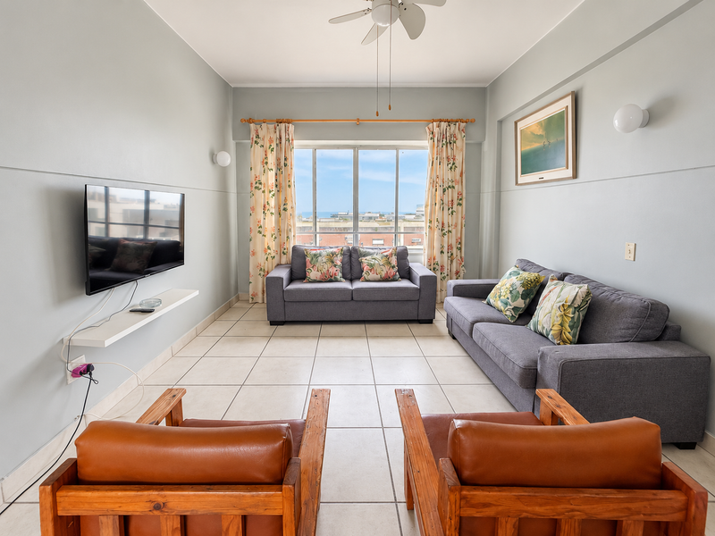 A bright living room featuring tiled flooring, a ceiling fan, and a large window with natural light and an exterior view.