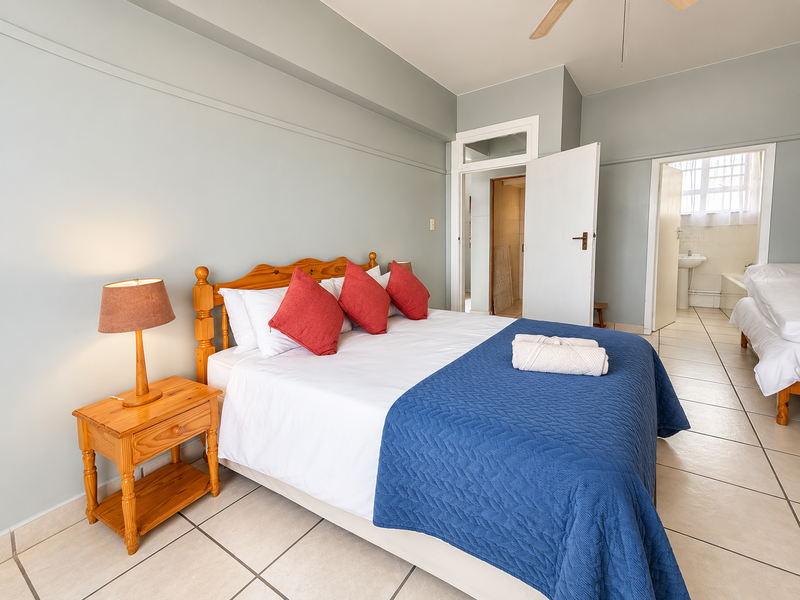 A spacious bedroom featuring neutral wall tones, tiled flooring, and a ceiling fan, with direct access to an adjoining bathroom.