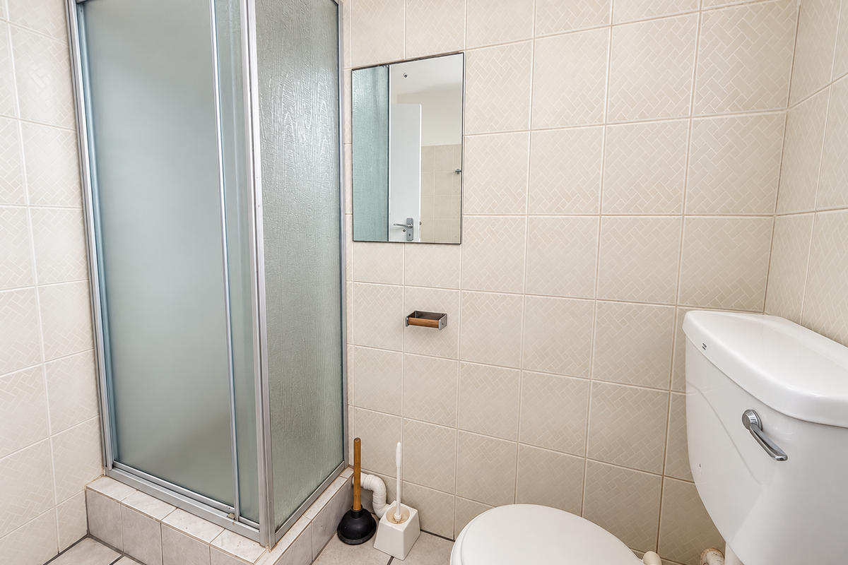 A functional bathroom featuring a shower enclosure, toilet, and wall-mounted mirror with neutral ceramic tiling throughout.