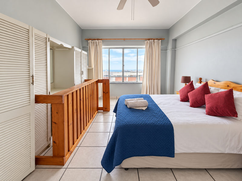 A bedroom featuring tiled flooring, a built-in wardrobe with louvered doors, a ceiling fan, and a window with views.