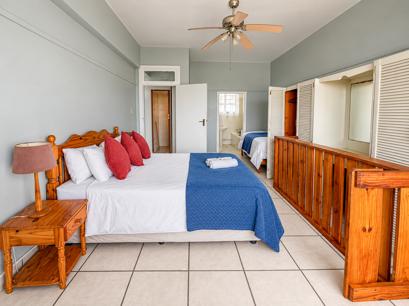 Spacious bedroom featuring tiled flooring, a ceiling fan, and built-in wardrobes with louvered doors, leading to an adjoining bathroom area.