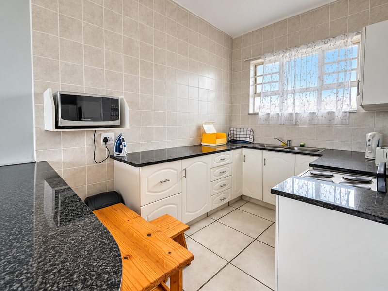 A functional kitchen featuring granite countertops, tiled backsplash, built-in cabinetry, and a double sink with ample workspace.
